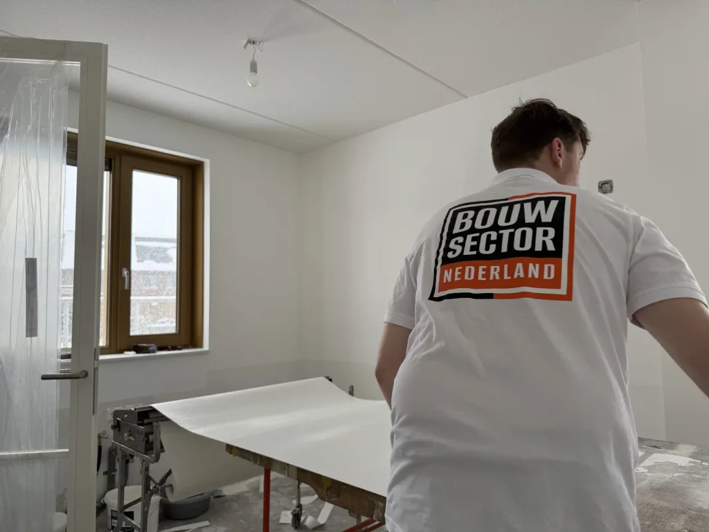 Behanger in wit poloshirt met logo legt een baan vlies klaar op de plaktafel