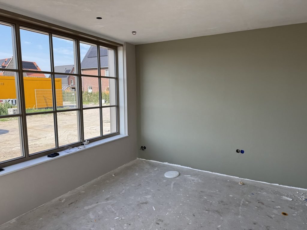 Kamer met een brede roedenpui en een wand die in grijsgroen is afgewerkt