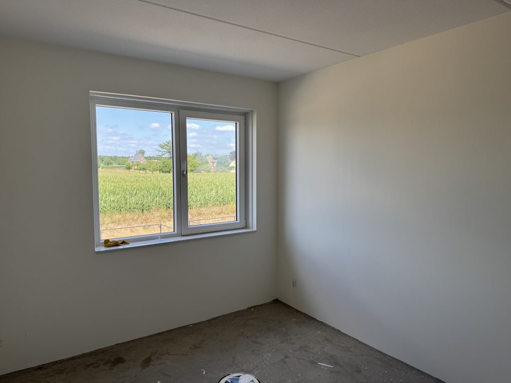 Slaapkamer met gladde lichte wanden en een raam dat uitkijkt over een maisveld