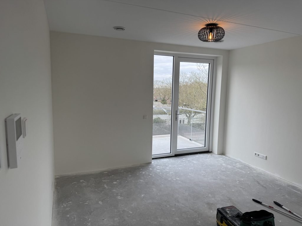 Lege kamer op een verdieping met openslaande deuren naar een balkon, wanden strak in lichte kleur